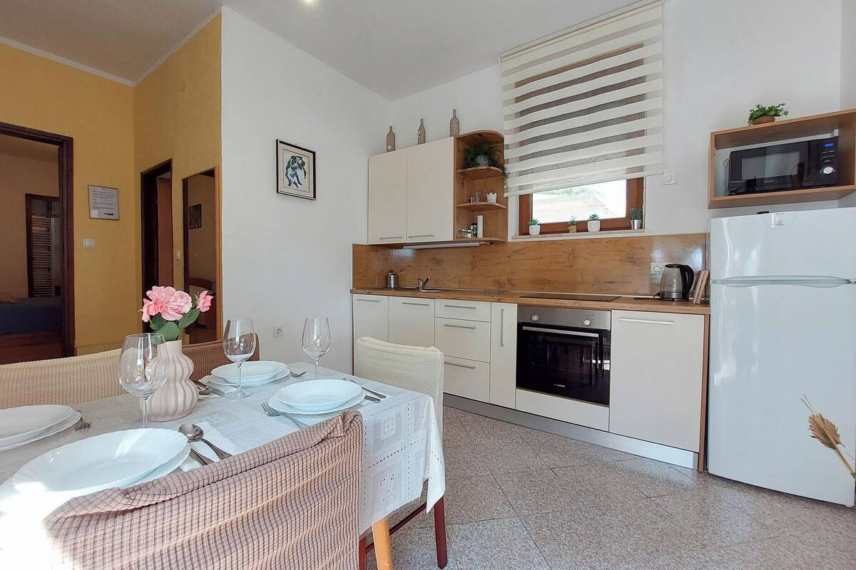 Una cocina moderna con armarios blancos, microondas y horno empotrado. Hay una mesa de comedor con platos y vasos.