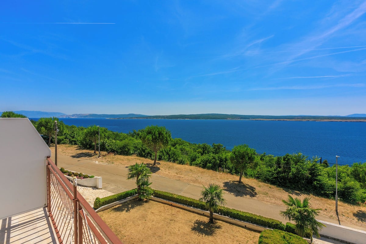 Un balcón con vistas a un paisaje costero, que incluye una carretera, vegetación y el mar.