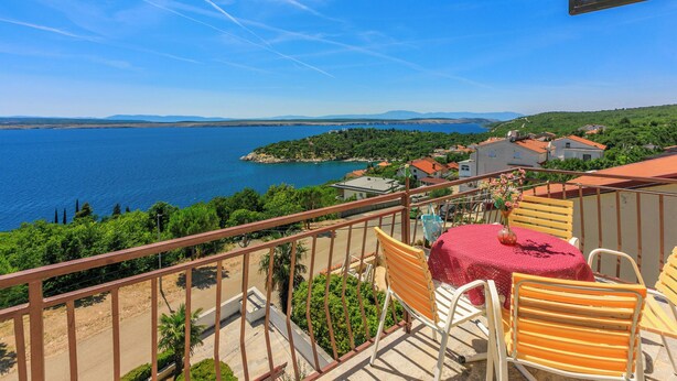 Un balcon donnant sur un lac, avec des chaises et une table agrémentée d’un vase de fleurs.