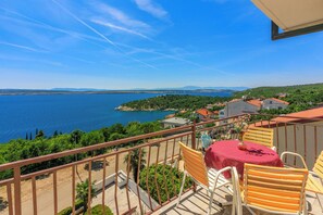 Un balcone con vista su un lago, sedie e un tavolo con un vaso di fiori.