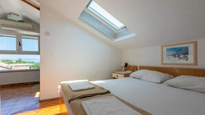 Une chambre avec une lucarne, un lit recouvert de draps blancs, une table de chevet et un tableau accroché au mur.