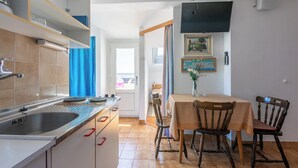 Une cuisine équipée d’un évier, d’une cuisinière et de placards, une table à manger avec des chaises, et un téléviseur fixé au mur.