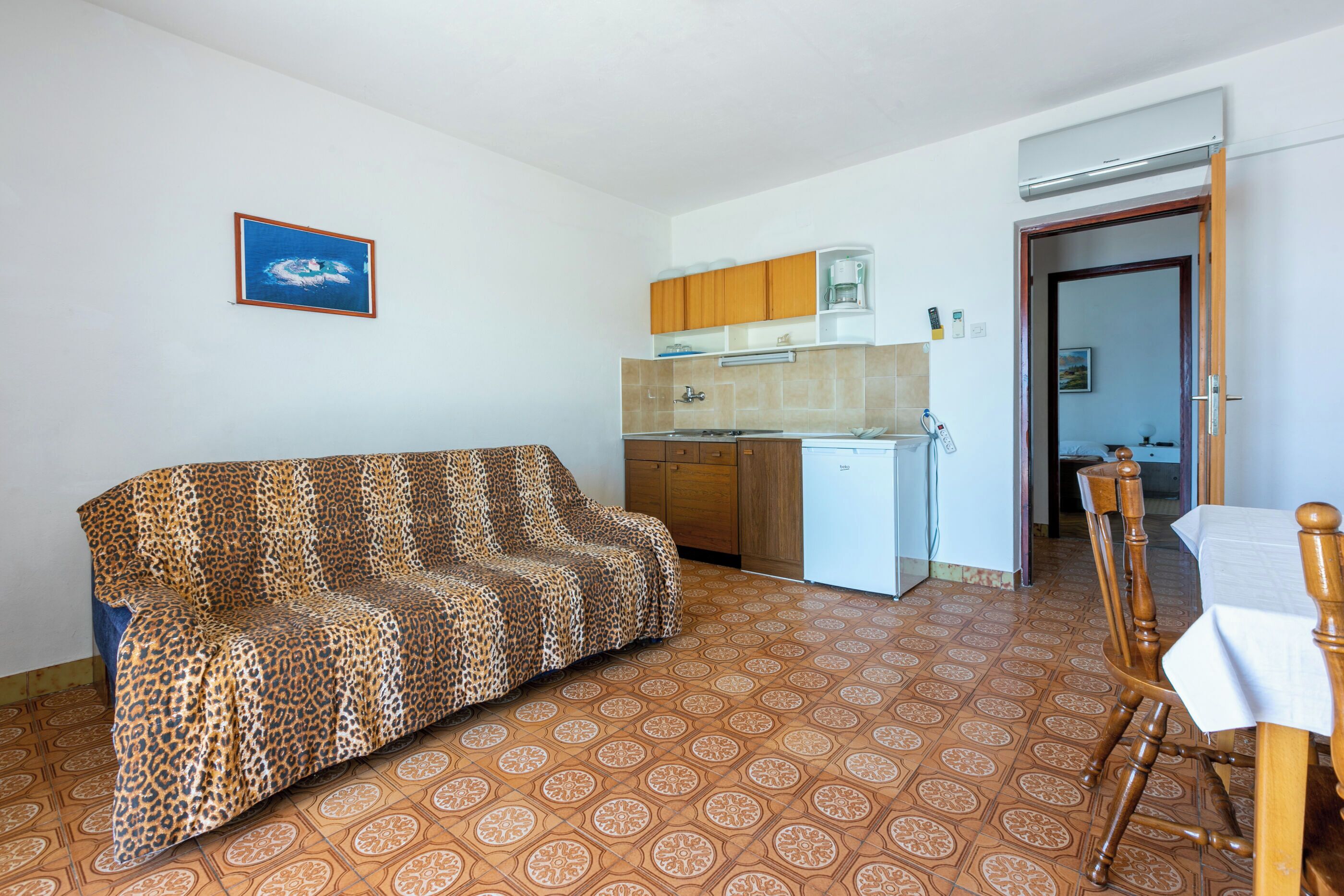 Un soggiorno con un divano a stampa leopardo, un tavolo da pranzo con sedie, una cucina con pensili e un frigorifero, e un pavimento decorato.