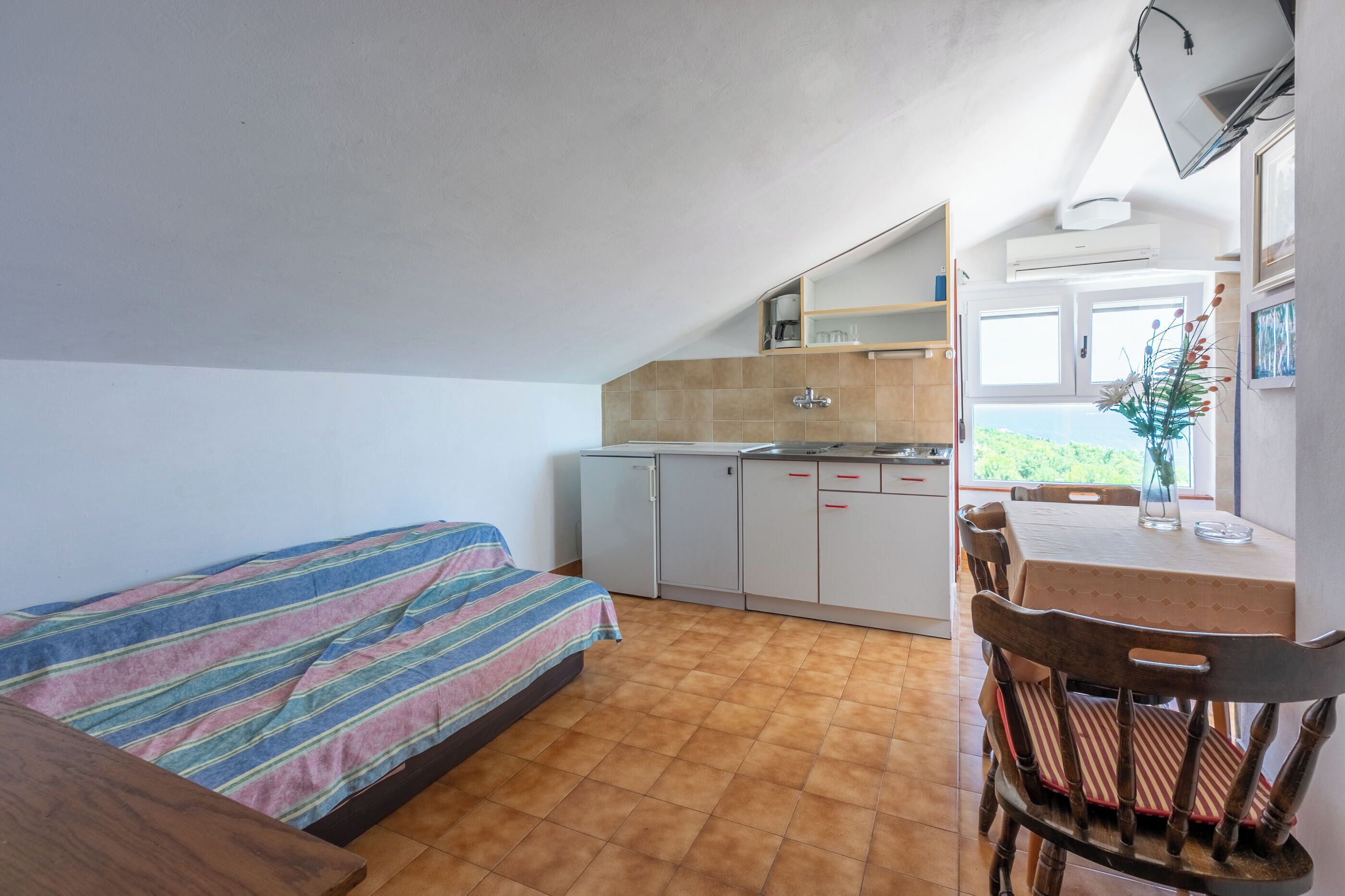 A compact room with a bed, a small kitchenette, a dining table, and a chair.
