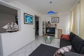 Una sala de estar con un sofá, una mesita con un florero, un barco modelo y un televisor.