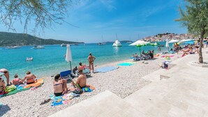 A beach with people sunbathing and swimming, boats in the water, and a town in the background. - Apartments Neno (Primosten)