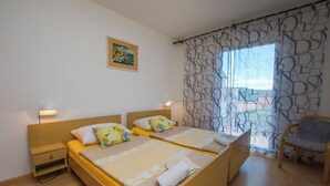 A double bed with a wooden headboard, a nightstand, a chair, and a window with patterned curtains. - Apartments Neno (Primosten)