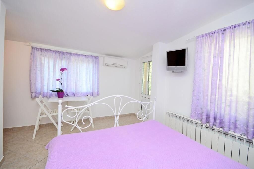 Un dormitorio con cama, escritorio, silla, planta en maceta y televisor en la pared.
