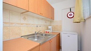 A compact kitchen with wooden cabinets, a stainless steel sink, and a white refrigerator. - Apartments Ivan Marina (Krk)