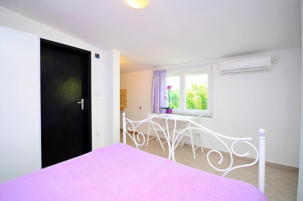 A bedroom with a bed, a window with curtains, a white radiator, and a door.