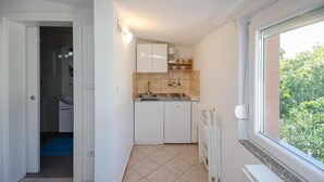 A compact kitchen with white cabinets, a sink, and a window with a view of greenery. - Apartments Ivan Marina (Krk)