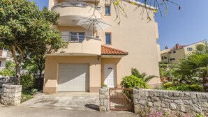 A two-story residential building with a white garage door, a balcony, and a stone wall with a gate. - Apartments Bella Vista (Srima)