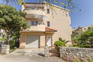 Un edificio residencial de dos plantas con una puerta de garaje blanca, un balcón y un muro de piedra con una reja.