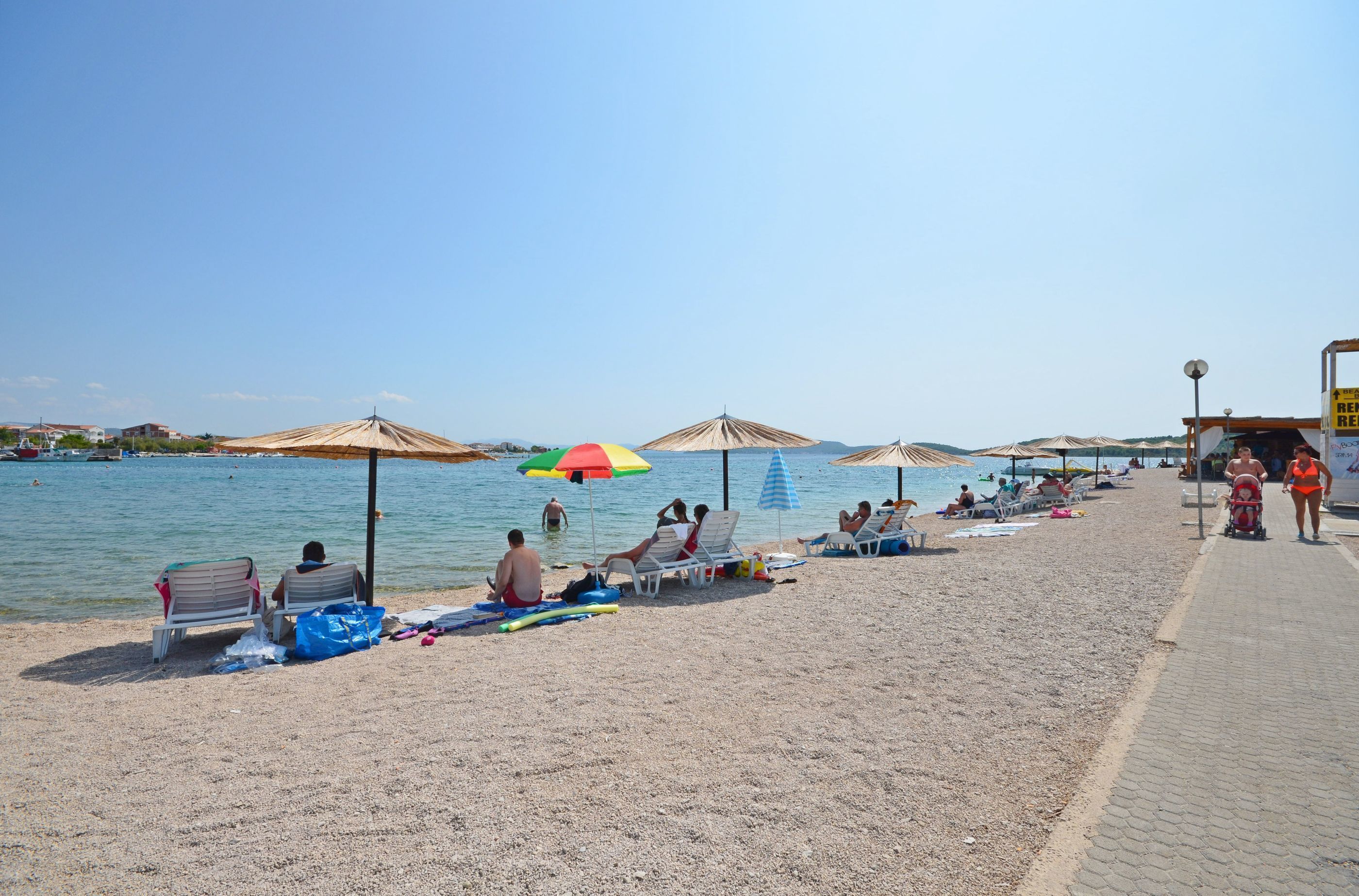 Een strand met ligbedden, parasols en een helder uitzicht op de zee.