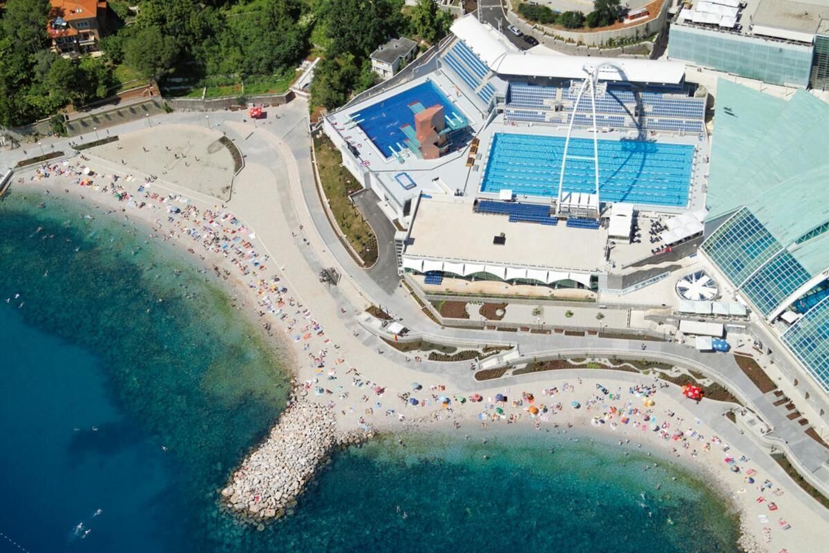 Ein Luftbild einer Küstenregion mit Schwimmbad, Strand und angrenzenden Gebäuden.