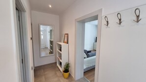 A hallway with a mirror, a potted plant, and a bed in the adjacent room. - Apartments Marija (Rijeka)