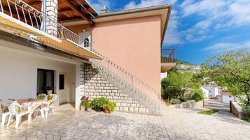 A stone-floored patio with outdoor furniture, a staircase with metal railings, and a building with a pink wall and a chimney.