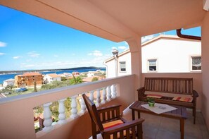 A balcony with a view of the sea and buildings, wooden furniture, and a lamp post. - Apartments Jasmin (Barbat)