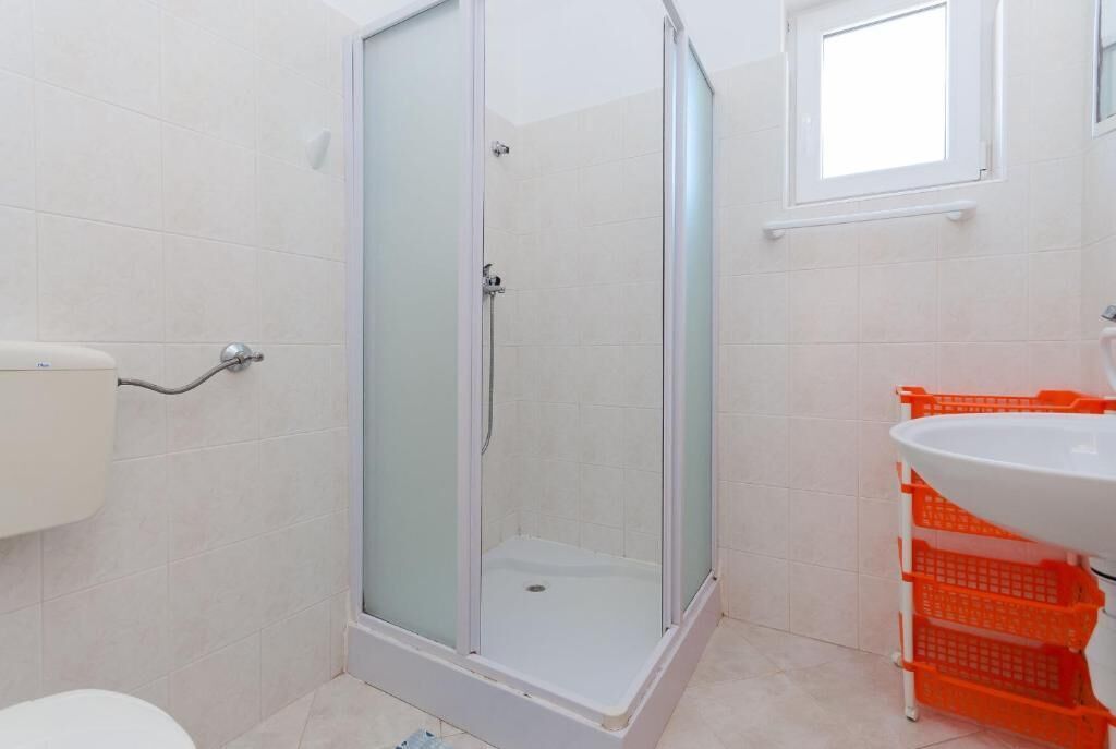 Un baño con ducha de vidrio, inodoro y lavamanos con cestas naranjas.