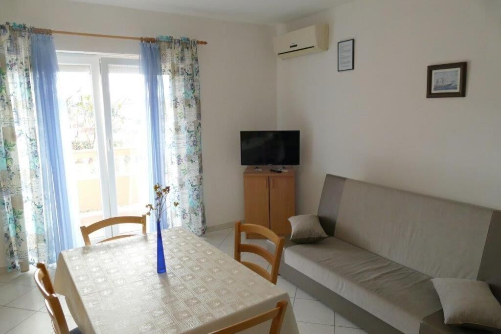 Een kamer met een eettafel, stoelen, een bank, een televisie op een kast en een raam met gordijnen.