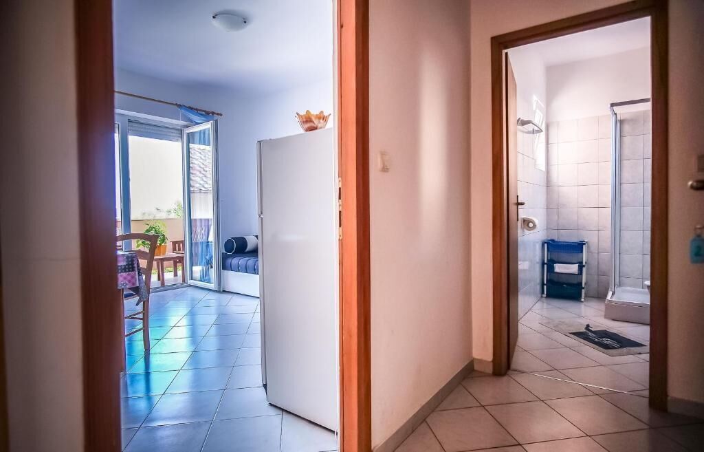 A hallway leading to a balcony with a refrigerator and a bathroom with a shower and toilet.