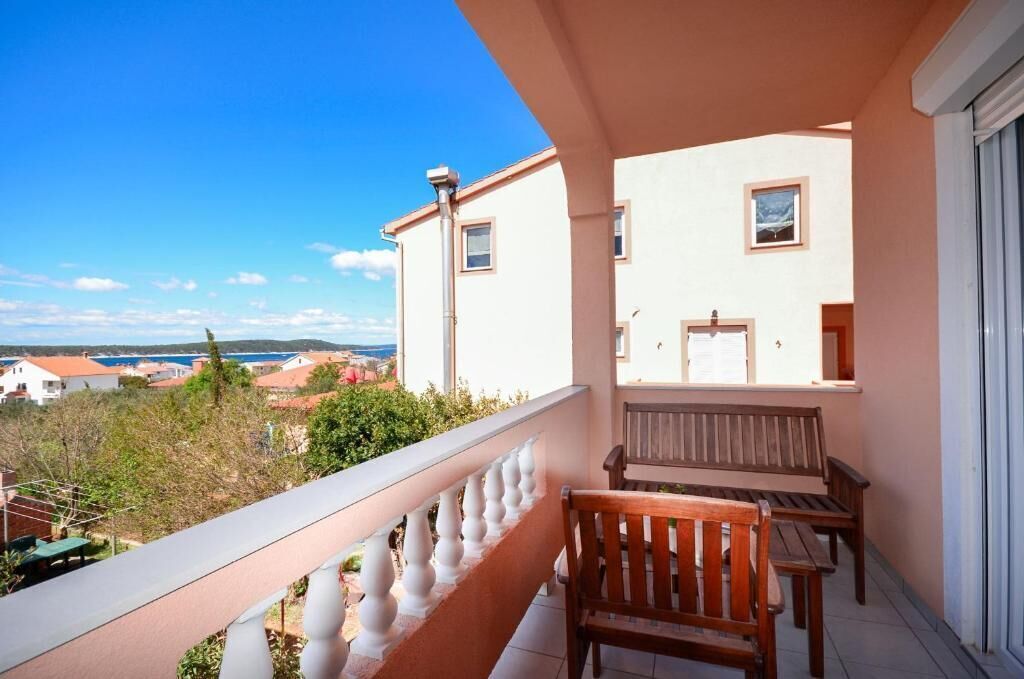A balcony with a wooden bench and a white balustrade overlooking a coastal town.