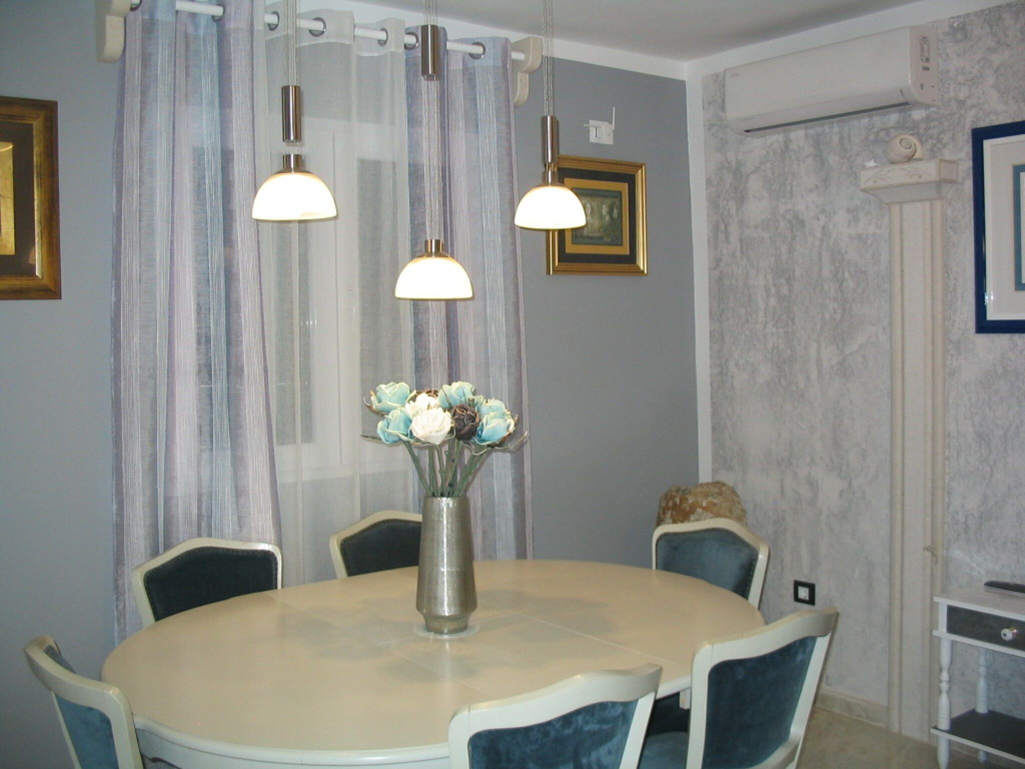 A dining area with a round table, chairs, a vase with flowers, and pendant lights.