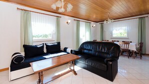 A living room with a black leather sofa, a wooden coffee table, and a dining area with a table and chairs. - Apartments Biserka (Barbat)