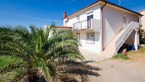 A two-story house with a balcony, a staircase, and a small garden with palm trees. - Apartments Biserka (Barbat)