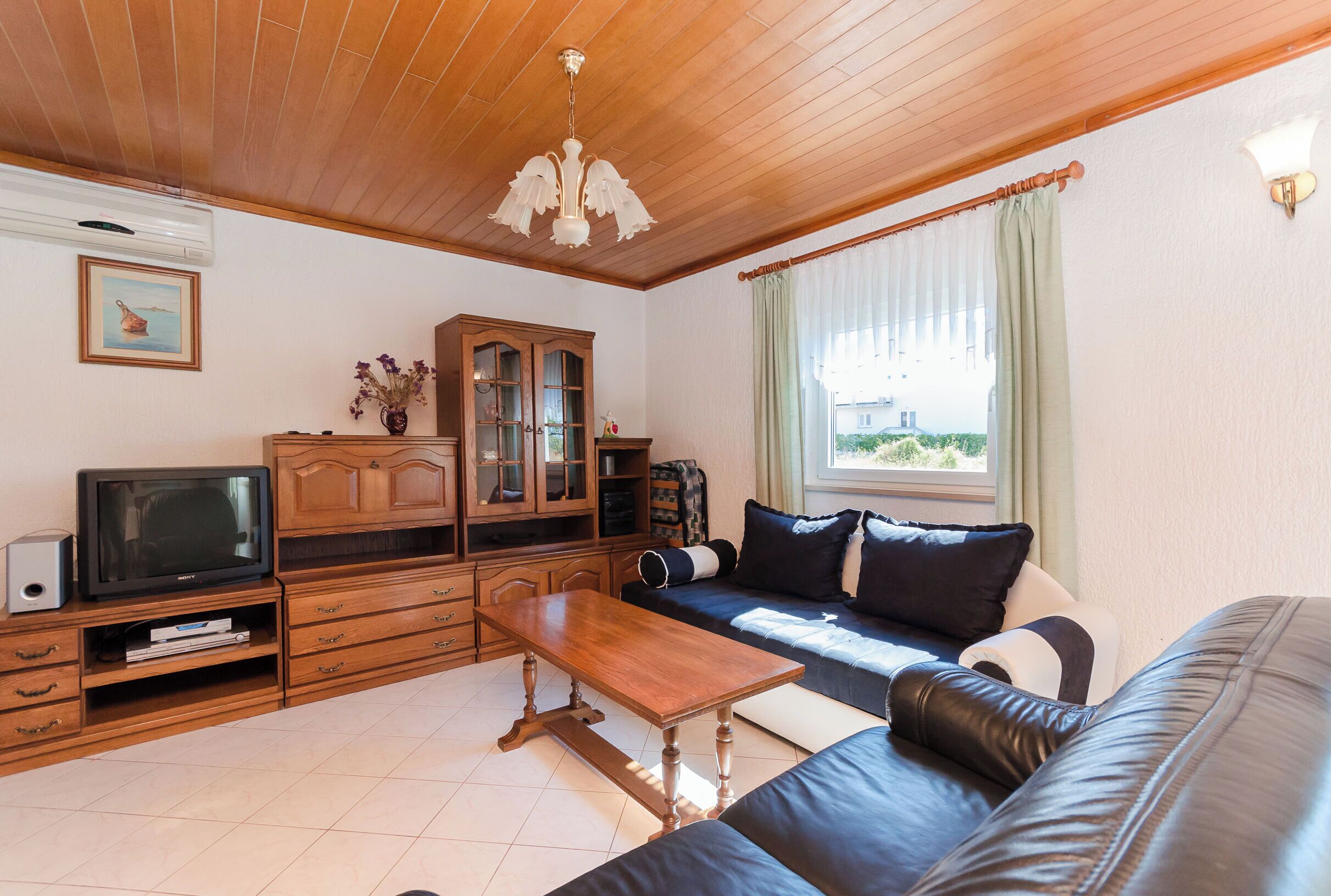 Una sala de estar con techo de madera, televisor, aparador, sofá y ventana con cortinas.