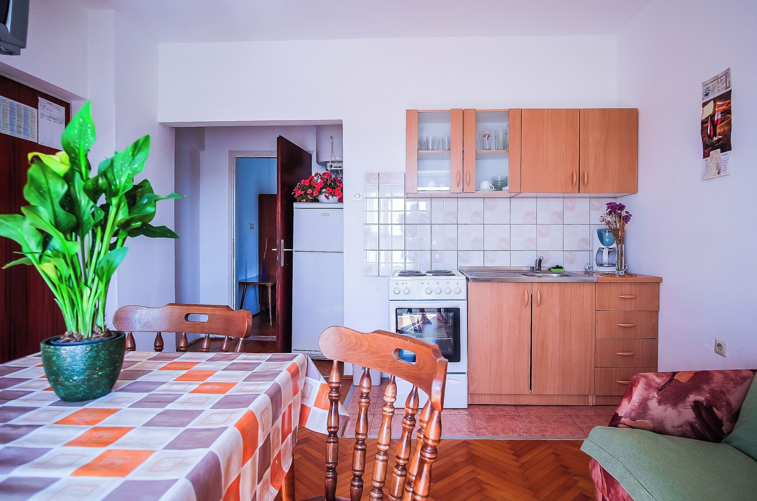 Une cuisine de taille réduite, avec des meubles en bois, une cuisinière et un évier. Une table à manger avec une nappe à carreaux et des chaises se trouve au premier plan.