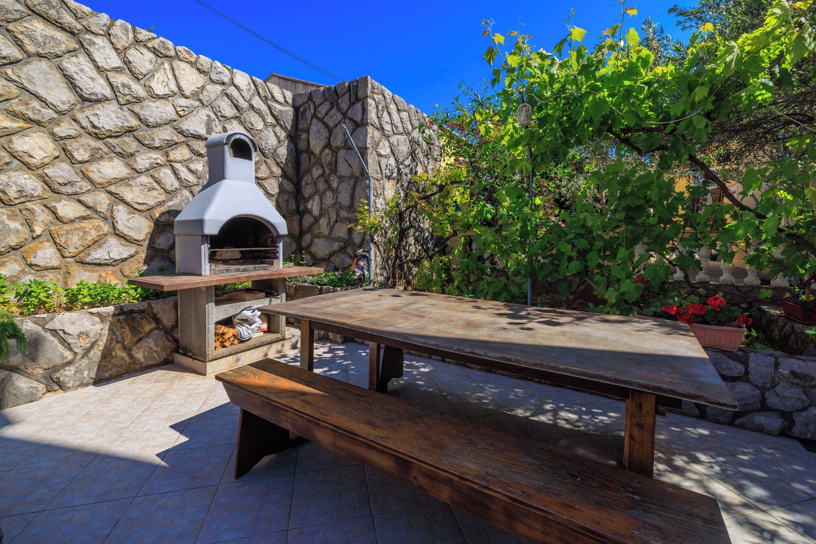 An outdoor patio with a stone wall, a pizza oven, and a wooden table.