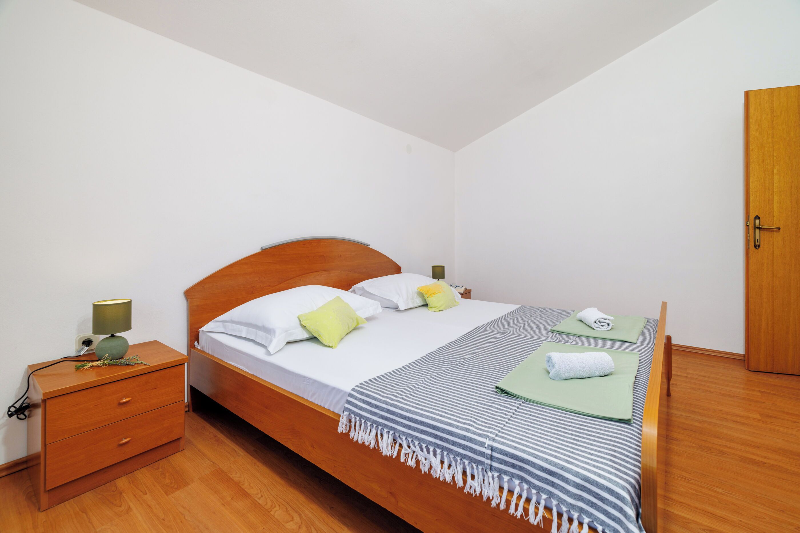 A neatly made bed with pillows, a bedside table with a lamp, and a wooden wardrobe.