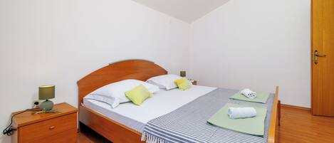 A neatly made bed with pillows, a bedside table with a lamp, and a wooden wardrobe.