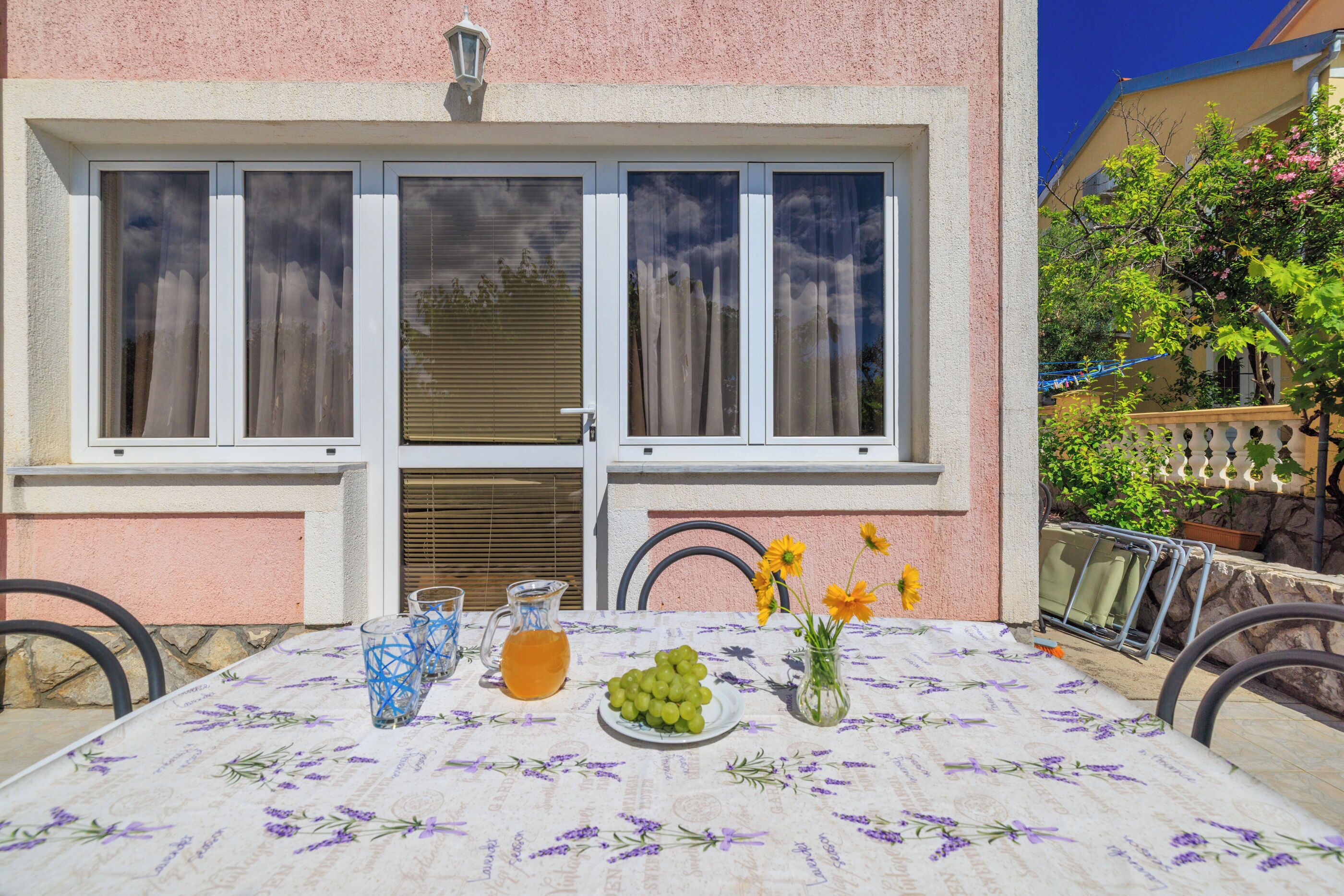 A table set with a floral tablecloth, a pitcher of orange juice, a plate of grapes, and a vase with flowers.