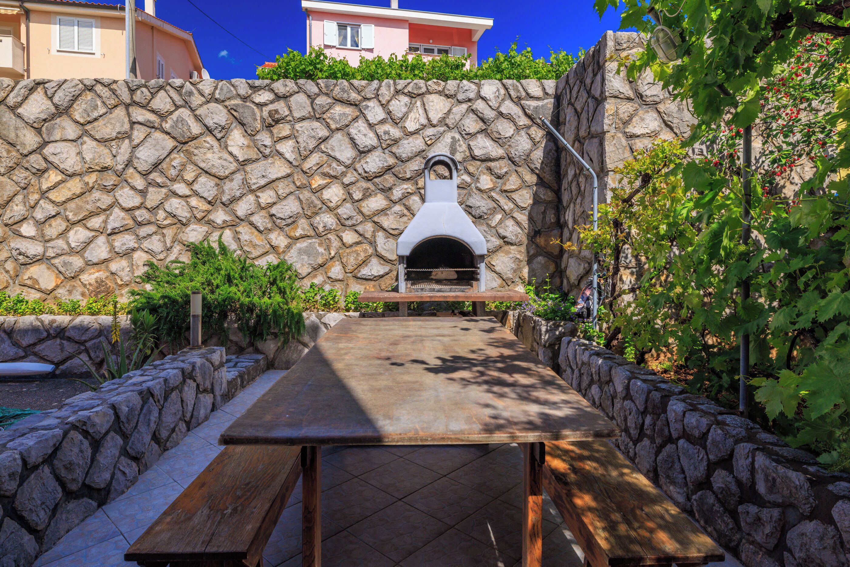 Un muro de piedra con un horno de pizza integrado y una mesa de picnic al frente.