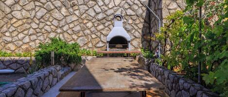 Un muro de piedra con un horno de pizza integrado y una mesa de picnic al frente.