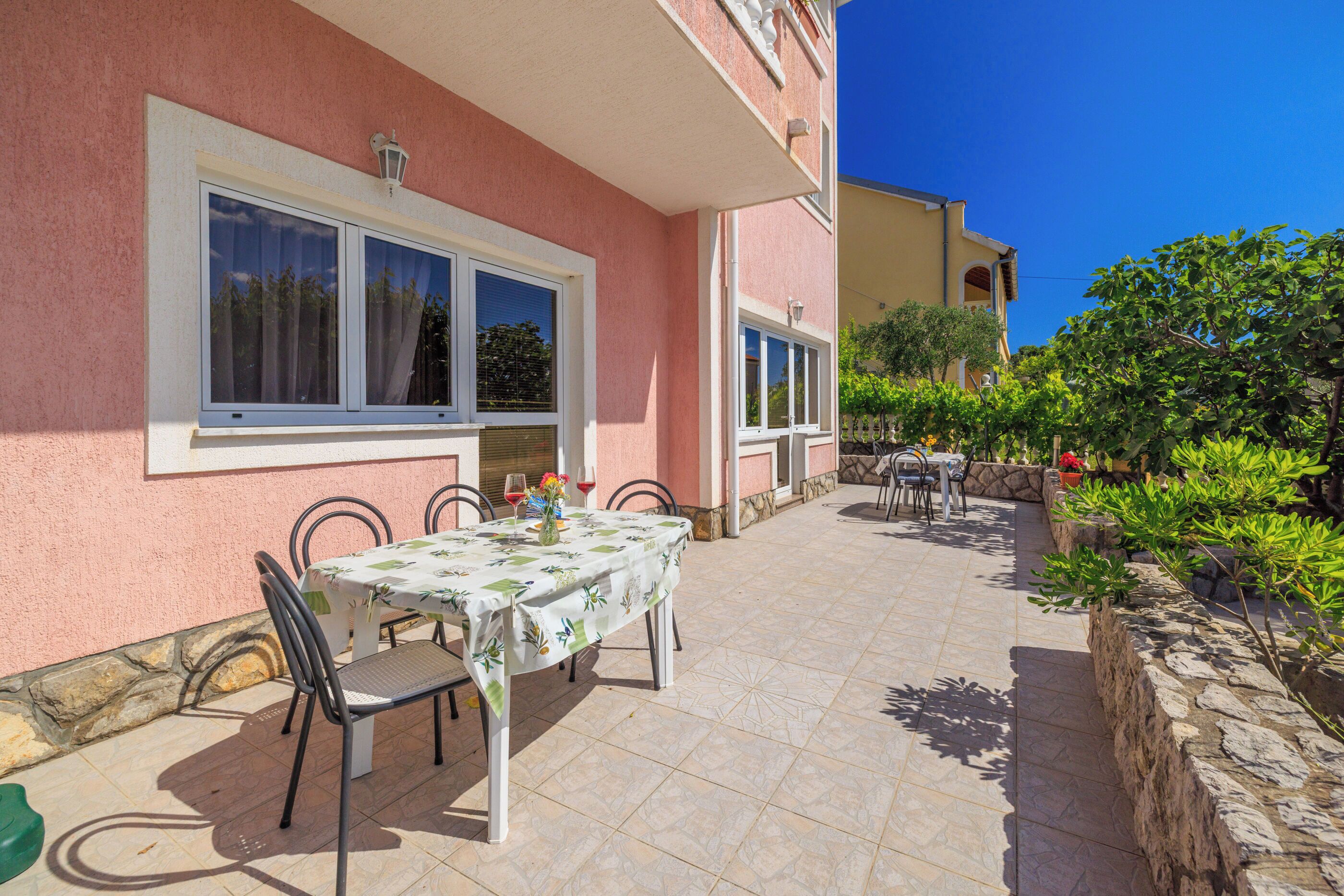 A patio with a table and chairs, a stone wall, and a building with pink walls and windows.