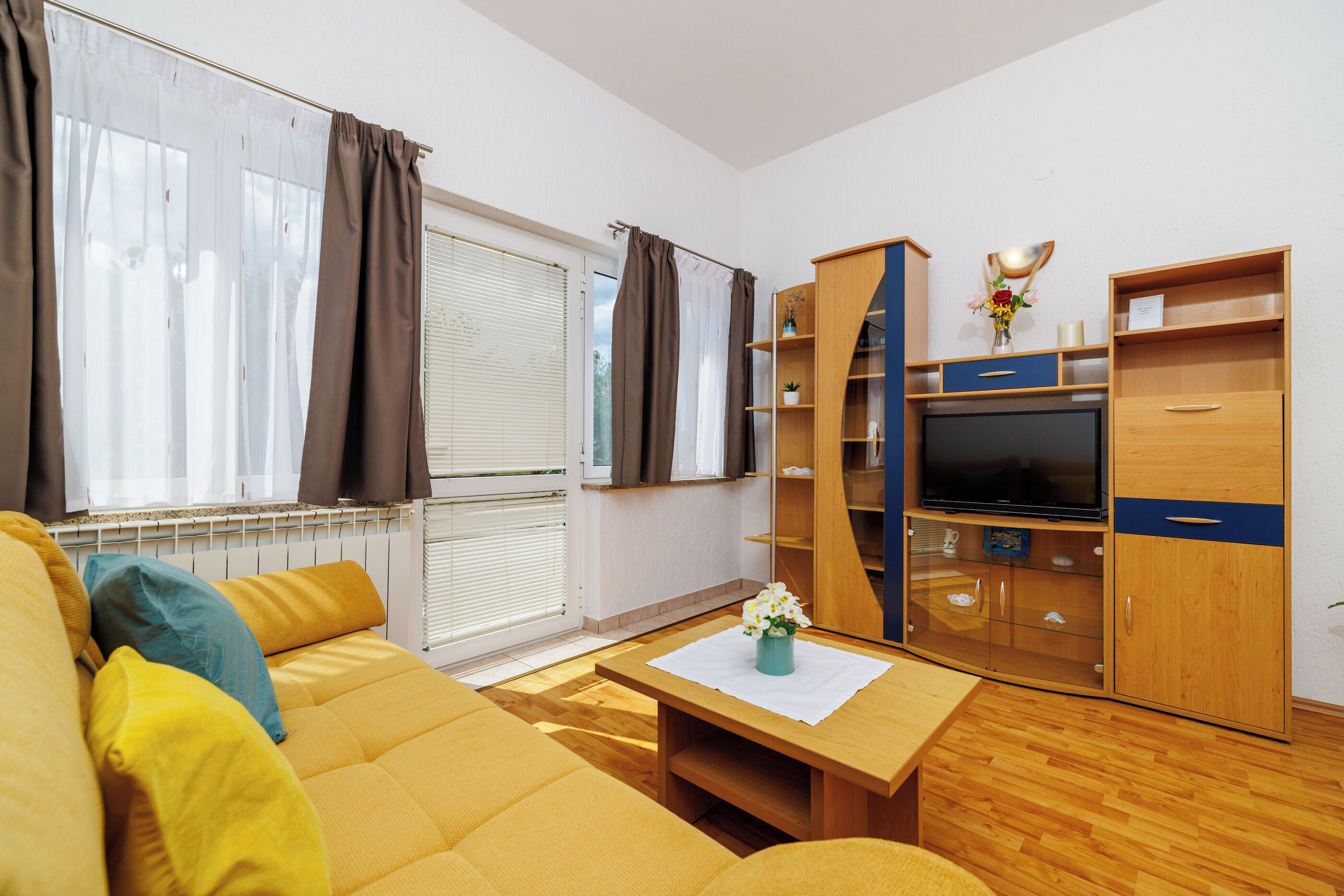 Una sala de estar moderna con un sofá, un televisor, armarios de madera y un ventanal con cortinas.