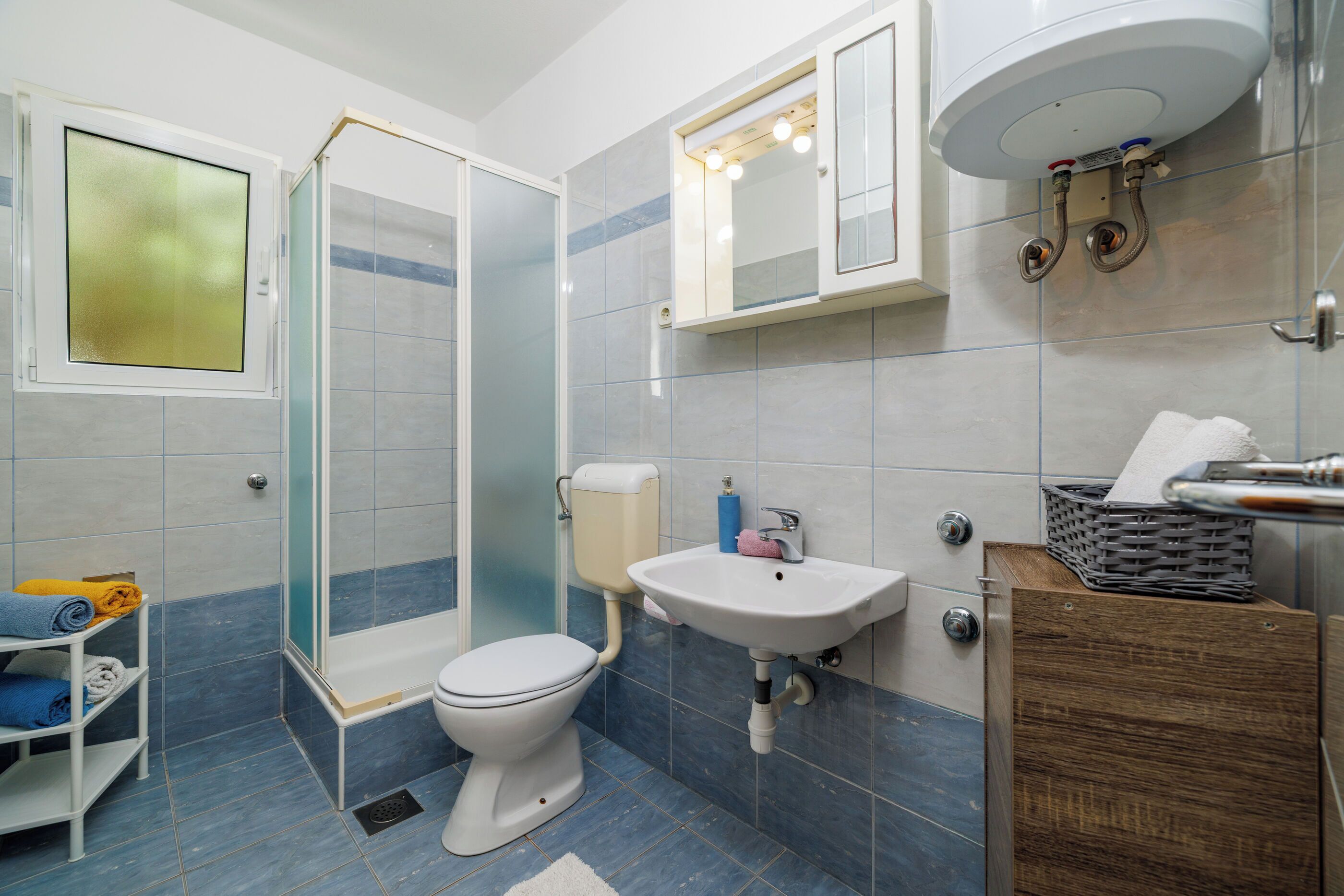 A modern bathroom with a glass shower enclosure, a white toilet, a sink with a mirror above, and a wooden cabinet.