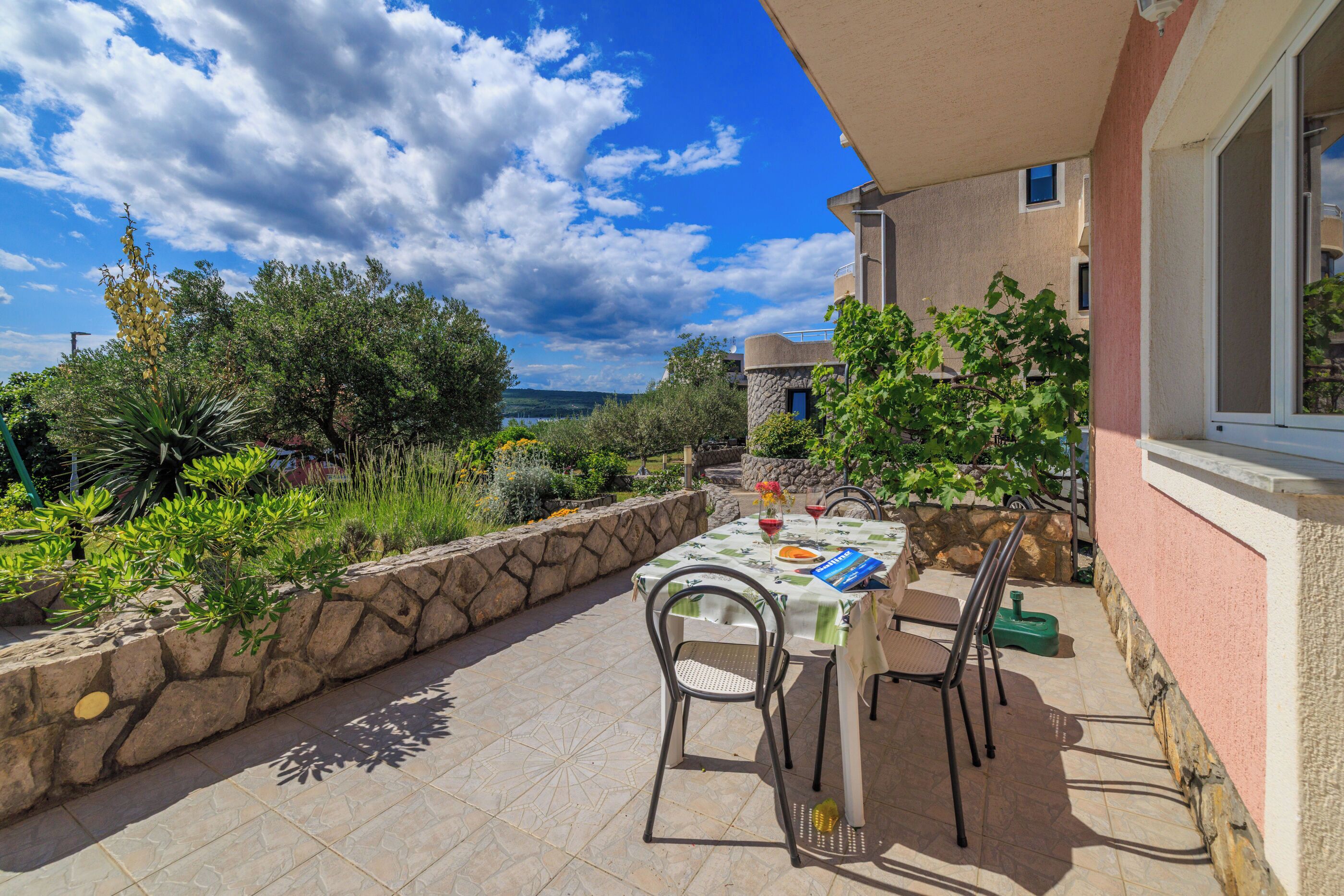 An outdoor patio with a table set for two, surrounded by stone walls and greenery.