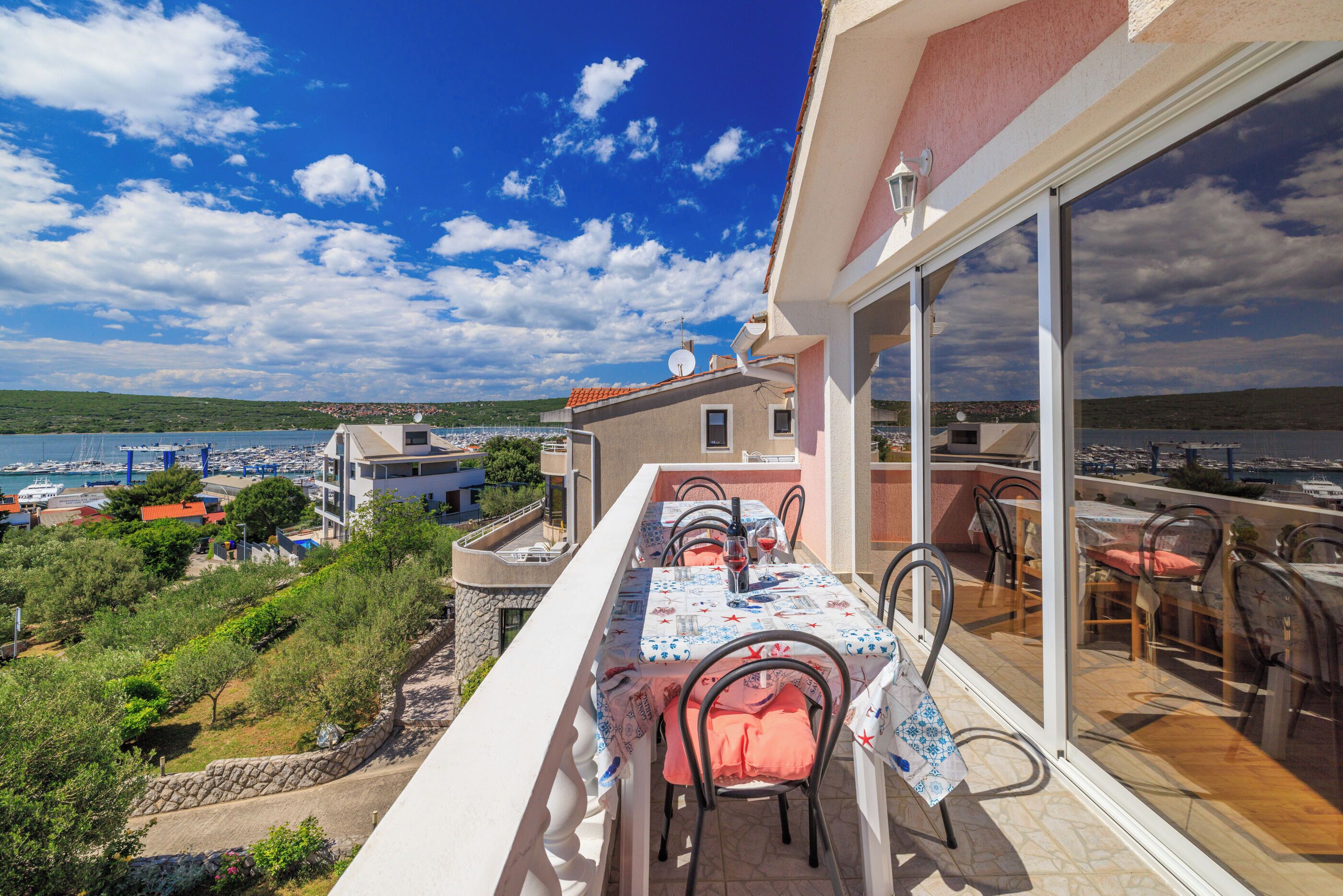 Un balcon avec une table dressée pour le dîner, donnant sur une marina et une étendue d’eau.
