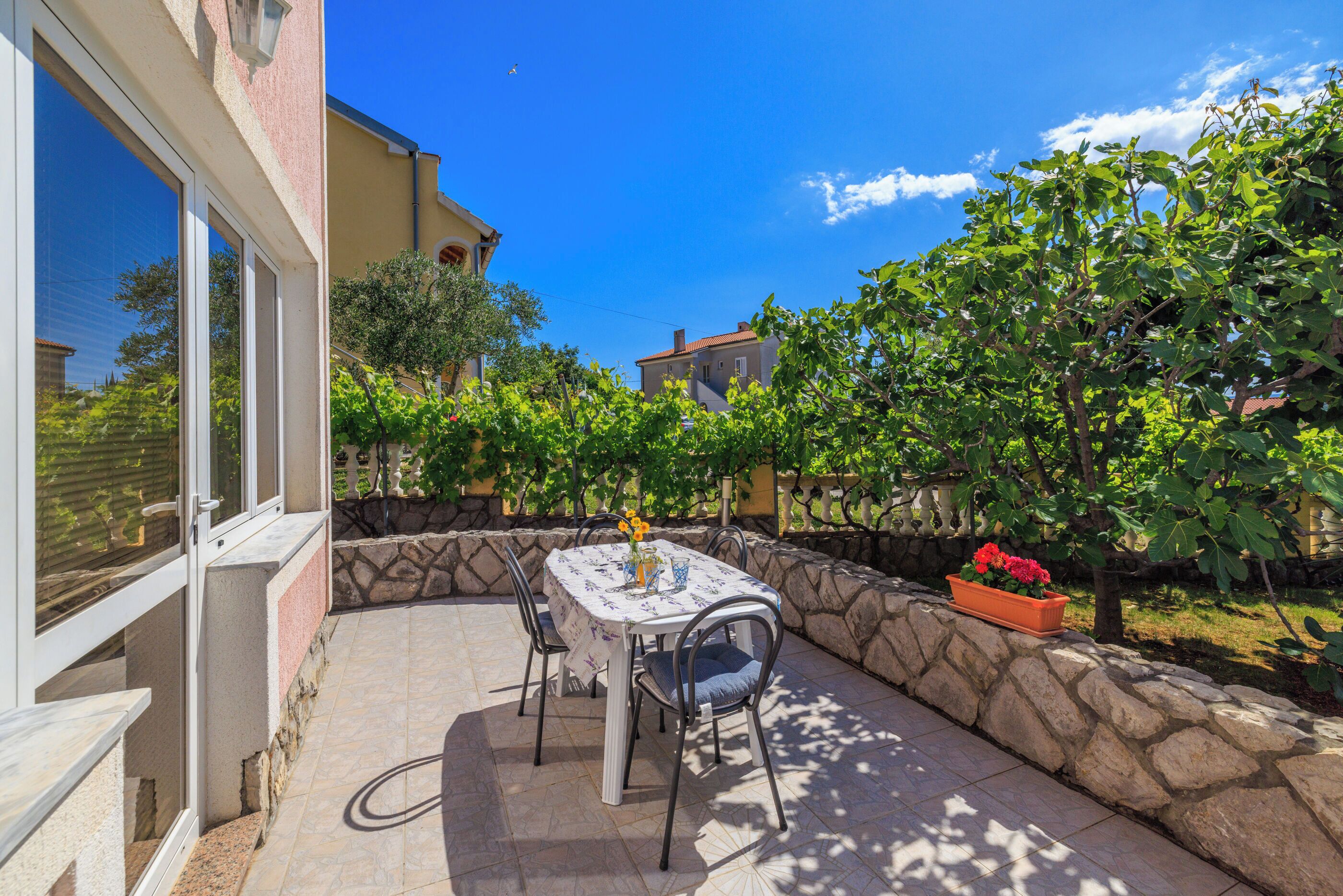 Une terrasse avec une table et des chaises, entourée d’un mur de pierre et de verdure.