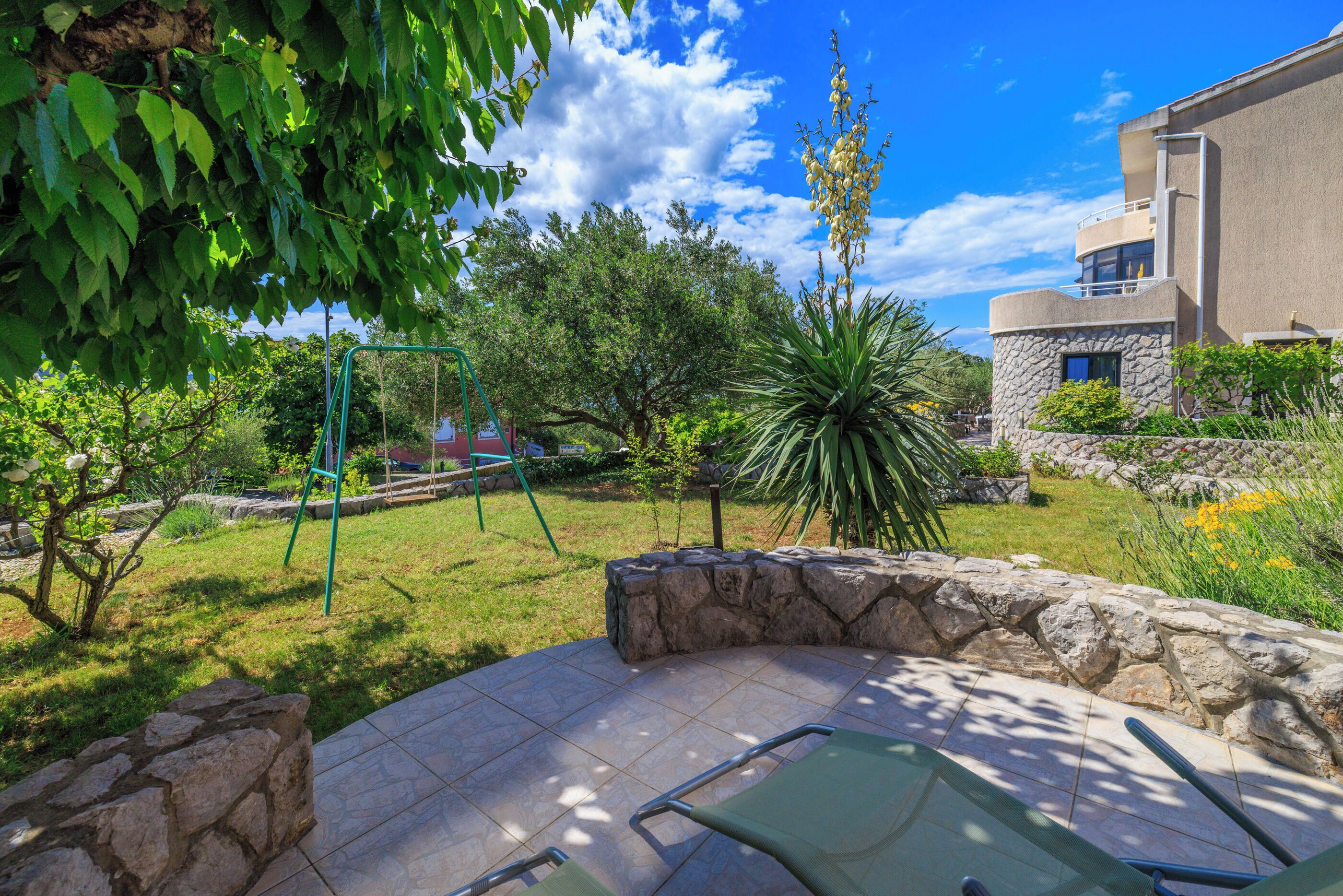 A patio area with a stone wall, a swing set, and a variety of plants.