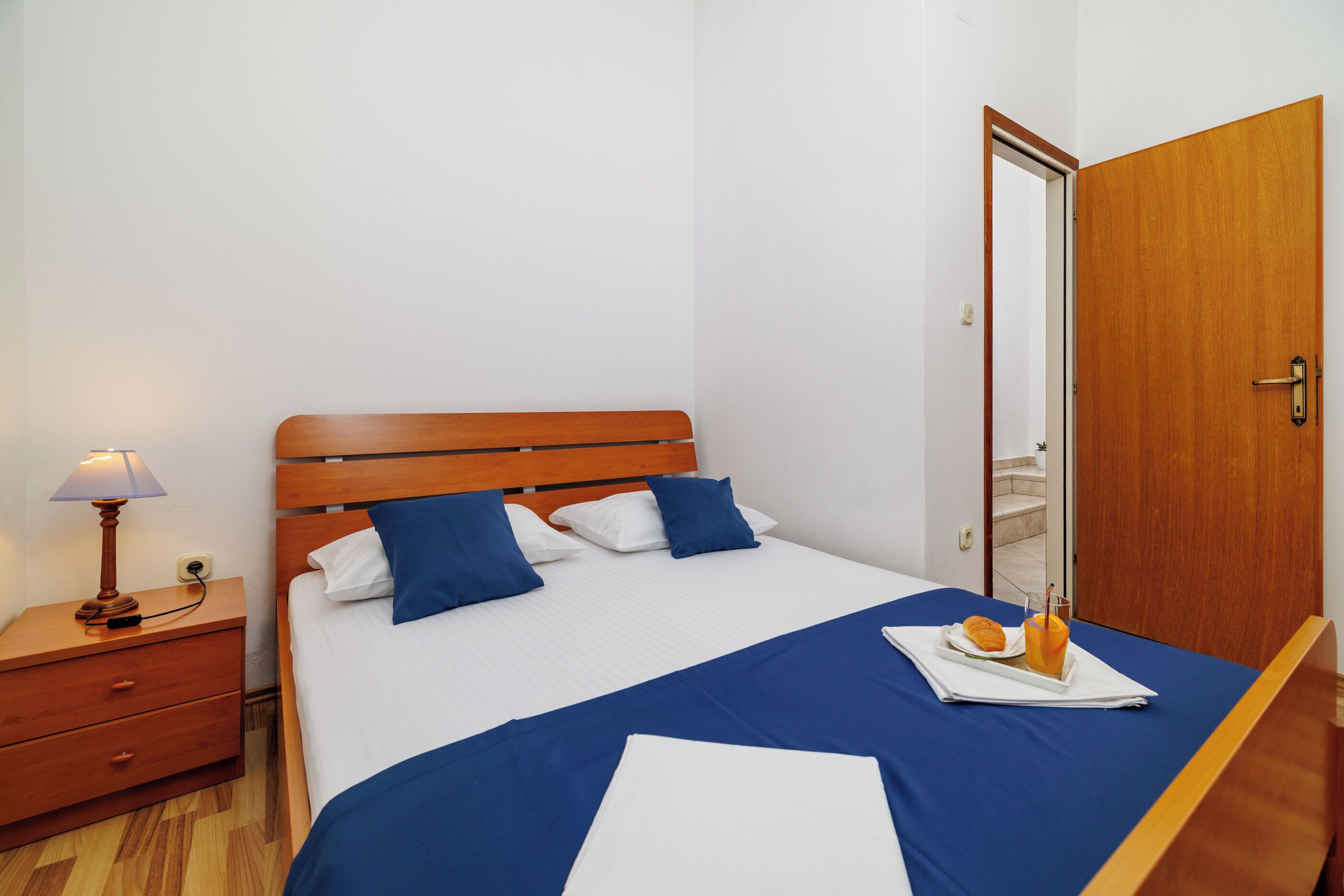 Un letto rifatto con lenzuola blu, una testiera in legno e un comodino con una lampada.
