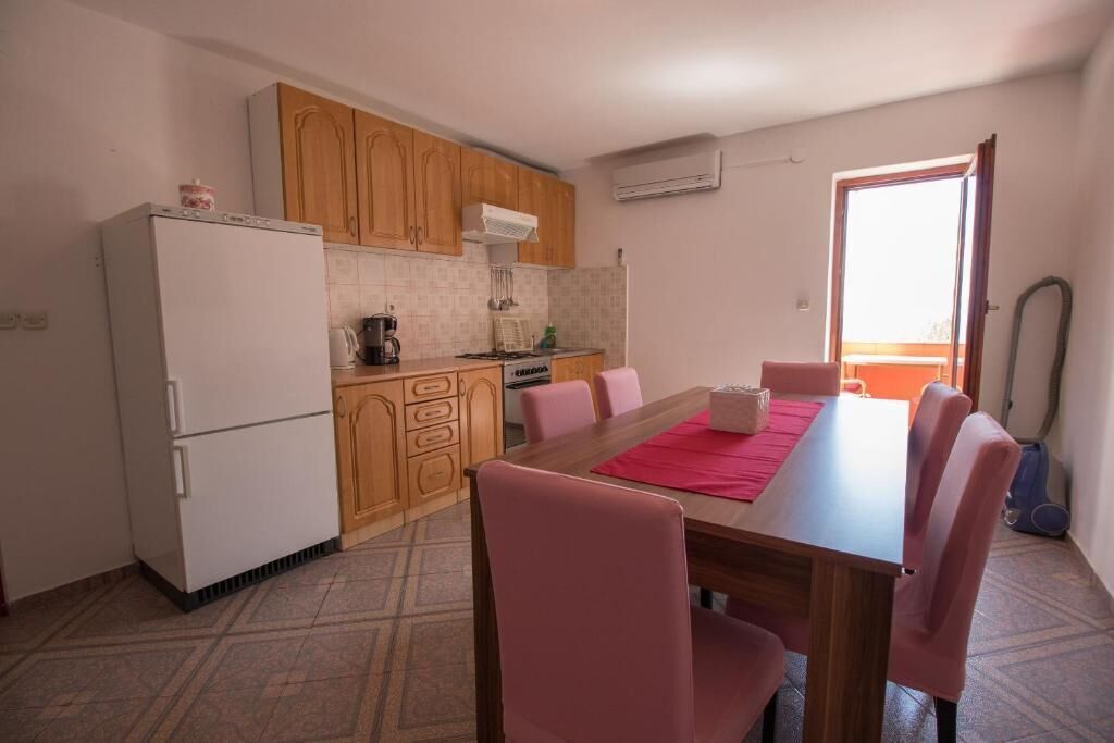 A compact kitchen with wooden cabinets, a white refrigerator, and a dining table with pink chairs.
