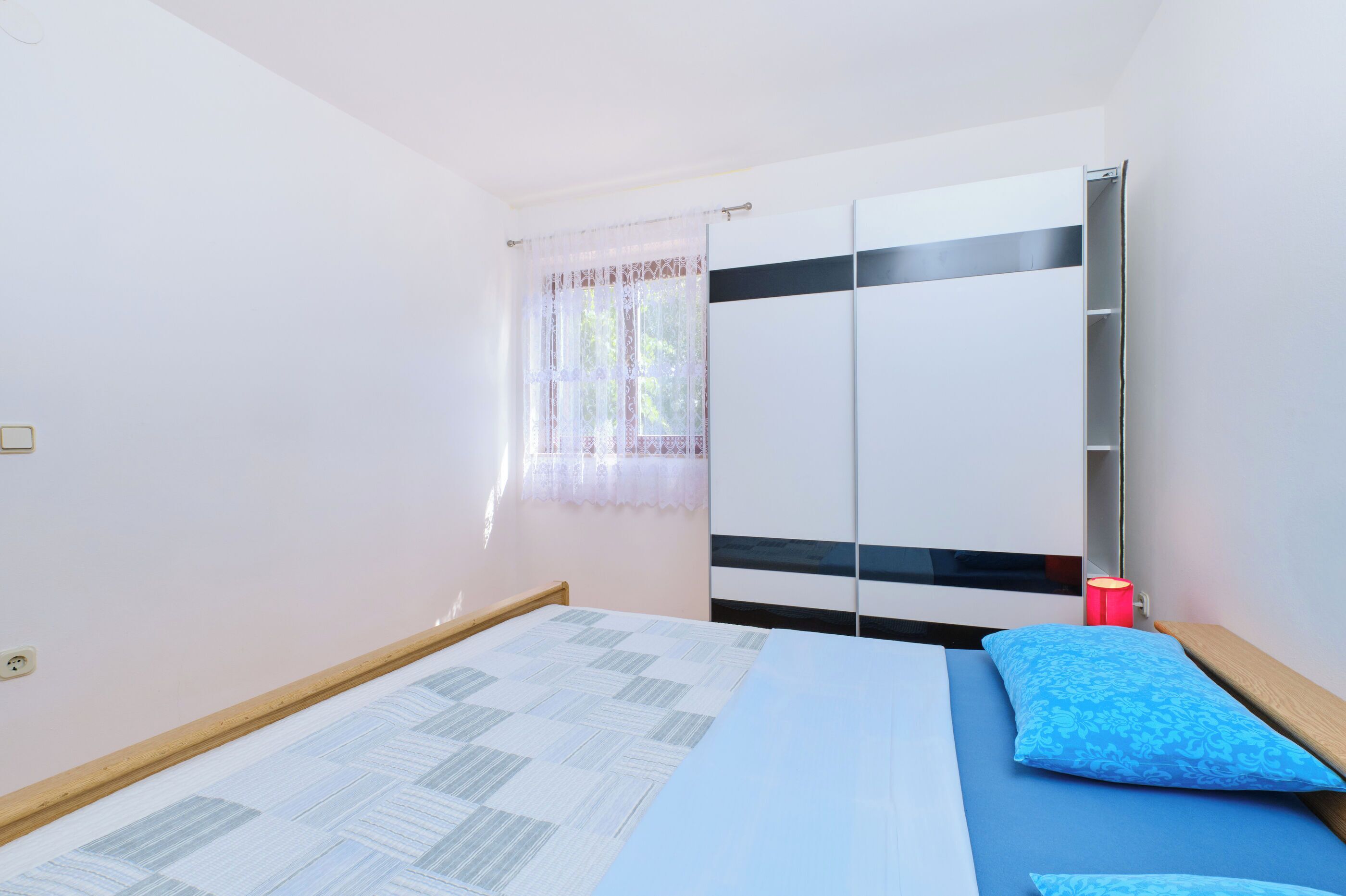 A bedroom with a bed, a bedside table, a nightstand, and a window with curtains.