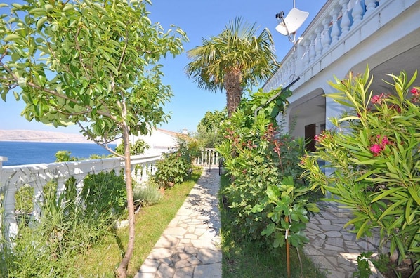 A stone pathway leading to a white building with a balcony overlooking the sea. - Apartments Lucia (Senj)