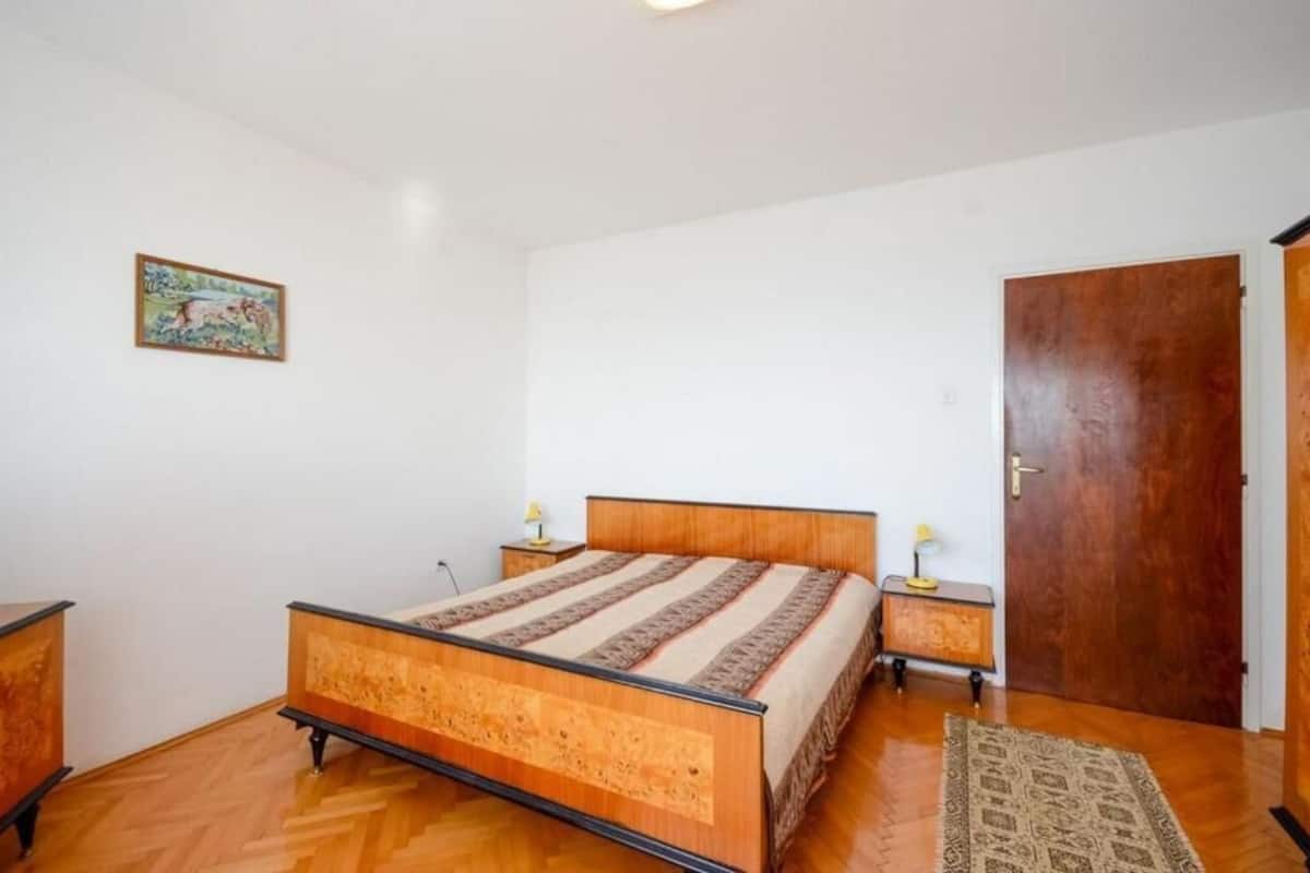 A bedroom with a wooden bed, bedside tables, a door, and a small rug.