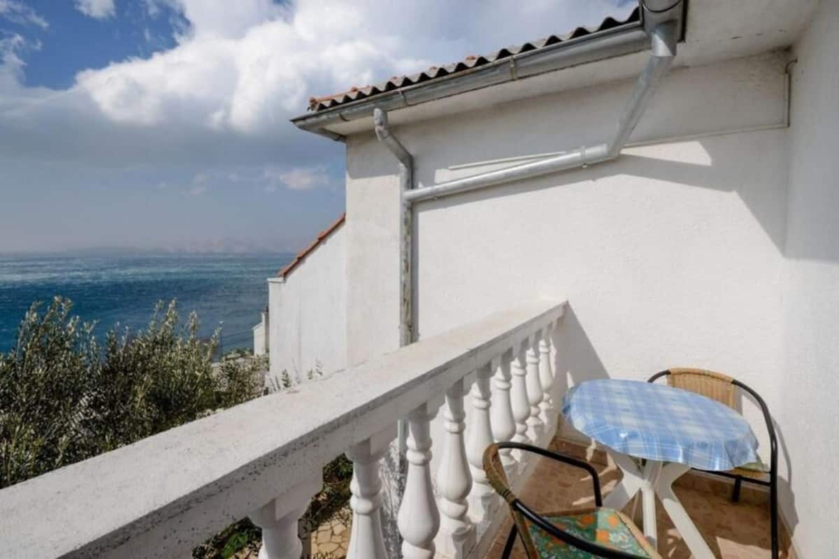A balcony with a white railing, a table with a blue tablecloth, and a view of the sea.